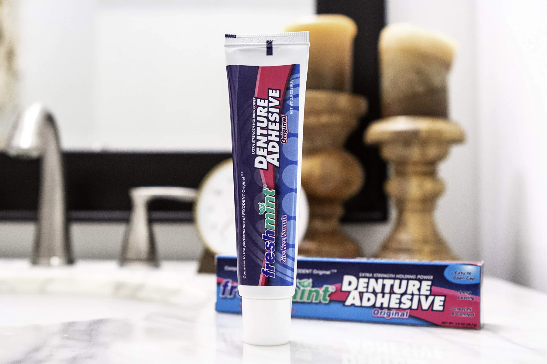 A Freshmint denture adhesive tube and carton on a bathroom counter